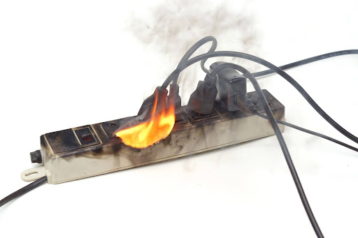 Surge protector on fire, with smoking appliance cords attached; a product liability lawyer handles cases arising from defective product malfunctions. Surge protector on fire, with smoking appliance cords attached; a product liability lawyer handles cases arising from defective product malfunctions.