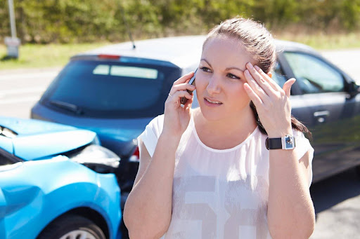 A woman making a phone call, standing in front of two vehicles damaged in a rear-end collision; notifying authorities is one of the first steps to take after an Uber accident. A woman making a phone call, standing in front of two vehicles damaged in a rear-end collision; notifying authorities is one of the first steps to take after an Uber accident.