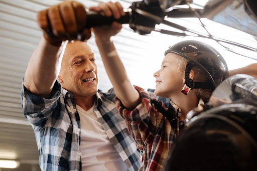 A father and his son riding a motorcycle; child motorcycle laws may impact when a child can ride with a parent. A father and his son riding a motorcycle; child motorcycle laws may impact when a child can ride with a parent.