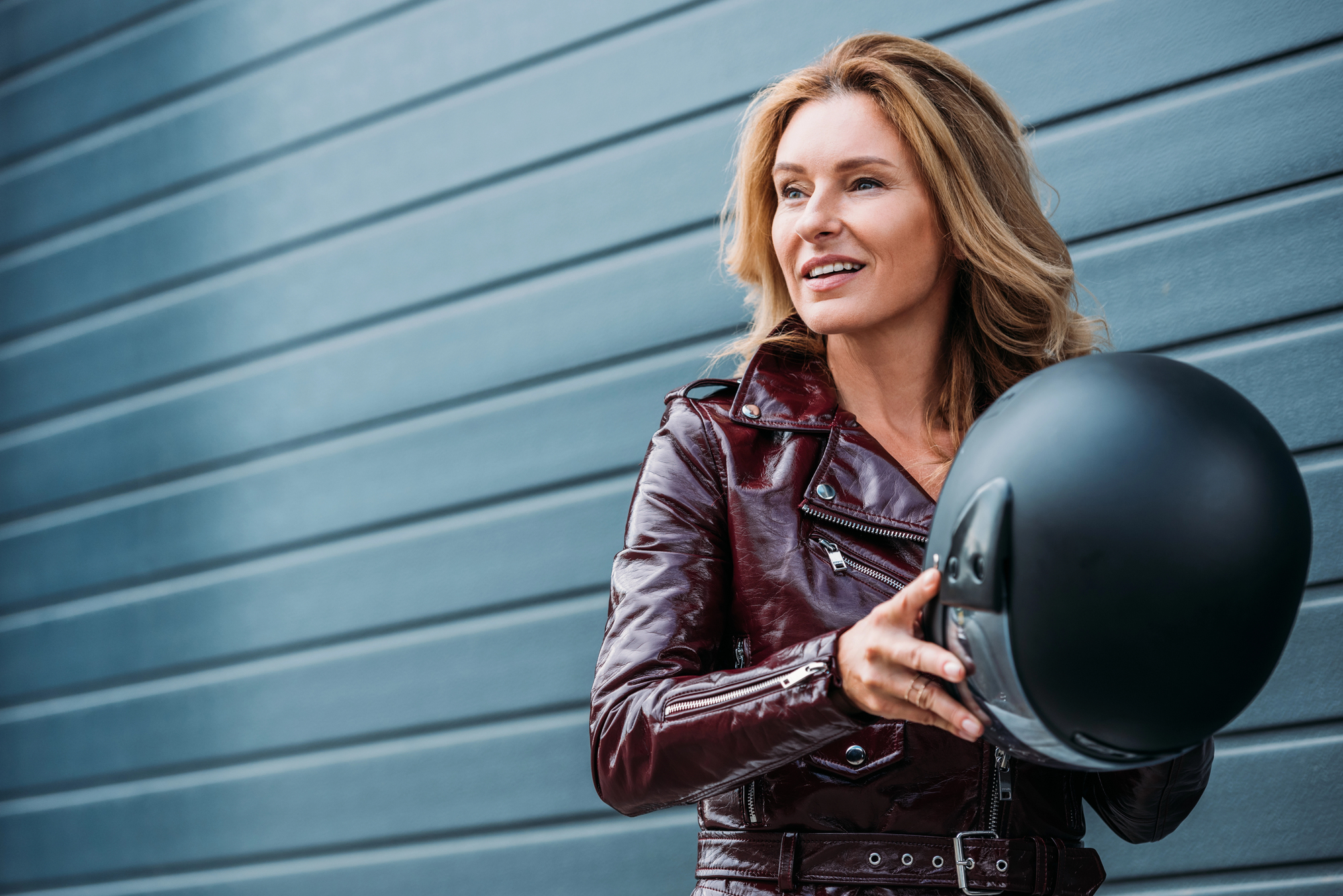 image1 A woman in a leather jacket holds a motorcycle helmet to wear, complying with motorcycle helmet laws.
