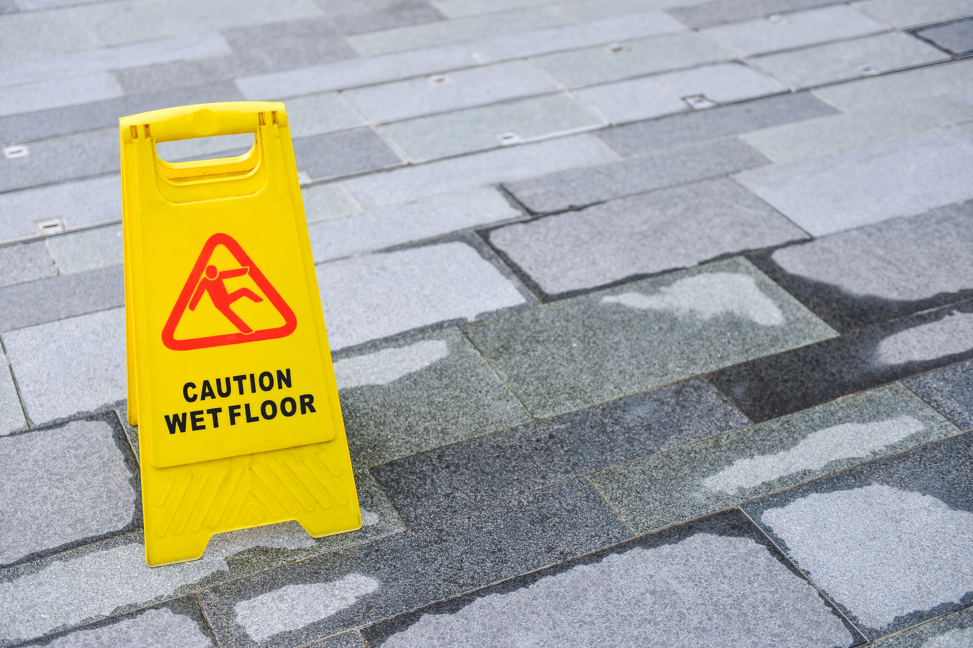 image1 Yellow caution wet floor sign on a tiled surface with visible water, illustrating a common slip and fall hazard in fall accident cases.